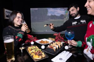 Grupo de ejecutivos disfrutando de una experiencia interactiva en simuladores de golf en Mulligan's durante una posada corporativa.